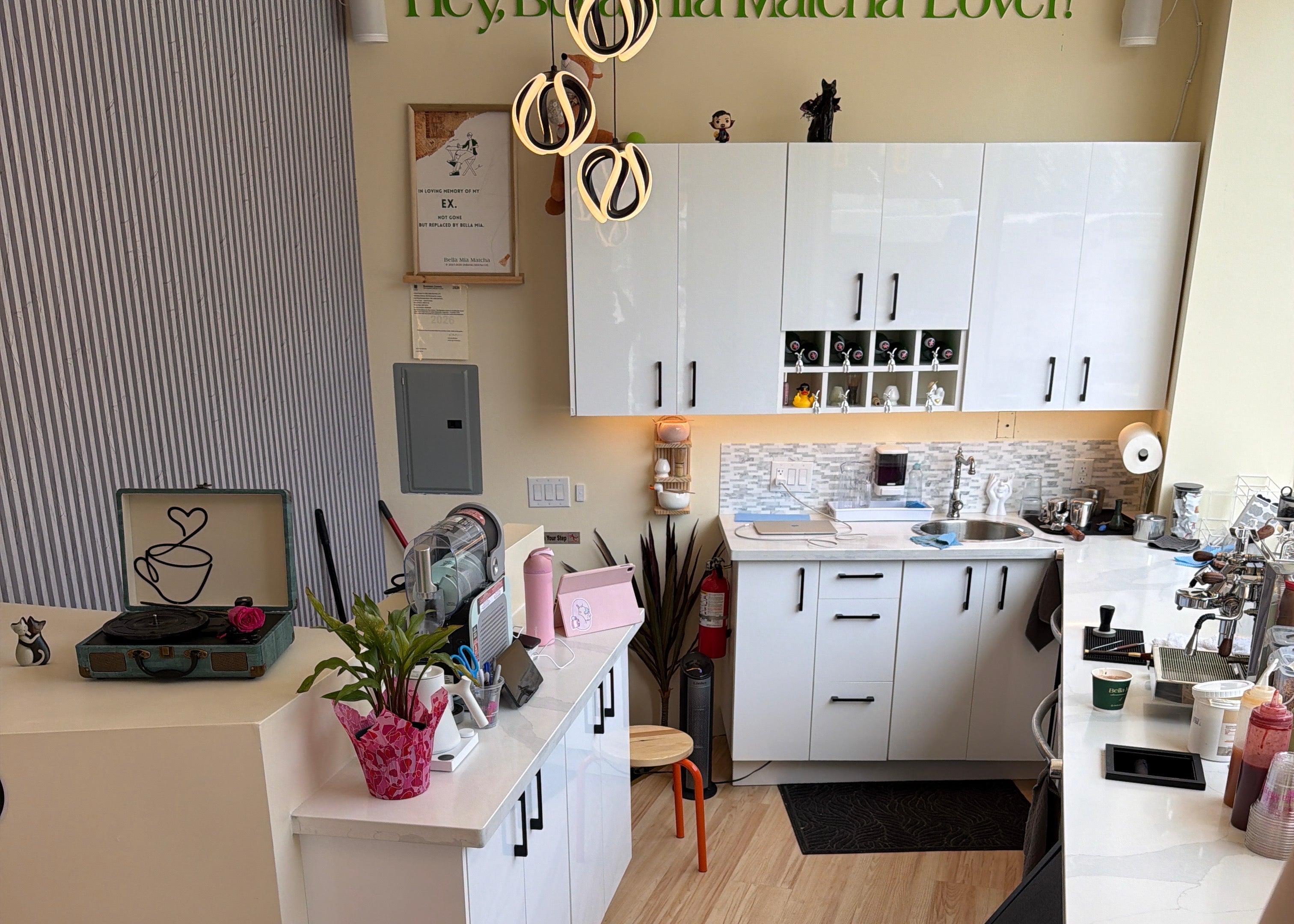 A high-angle, sideways view of a modern kitchen of Bella Mia interior featuring white cabinets, light wood flooring, black countertops, and various kitchen appliances and accessories.